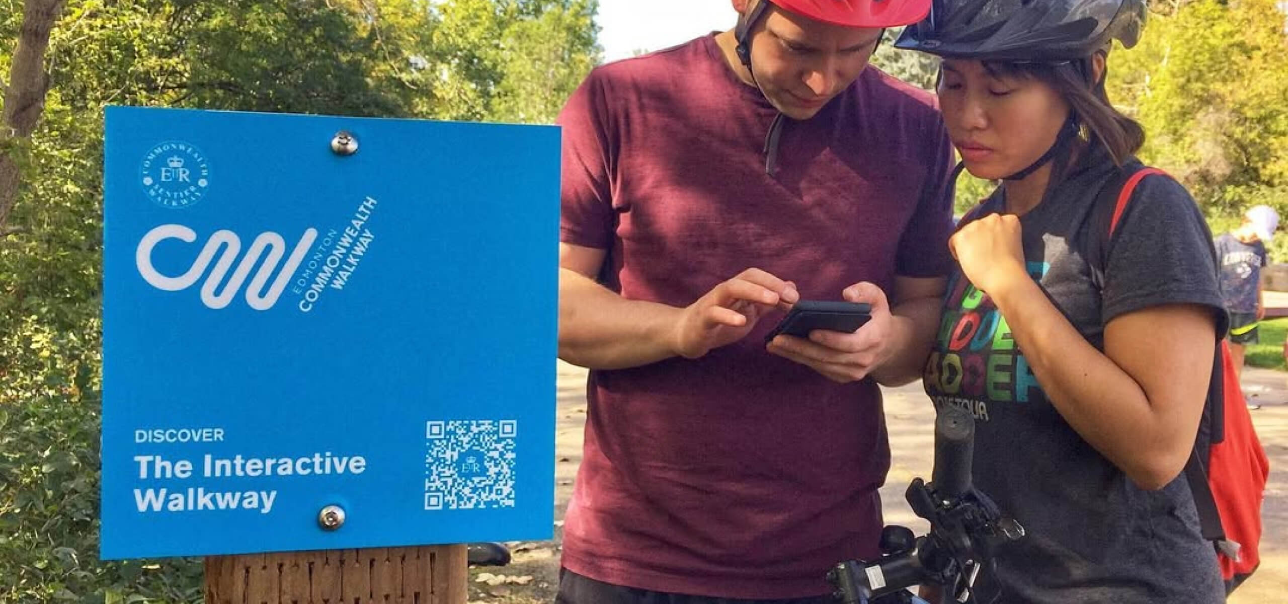 A photo of two cyclists out in Edmonton's river valley using the Commonwealth Walkway app alongside physical signage