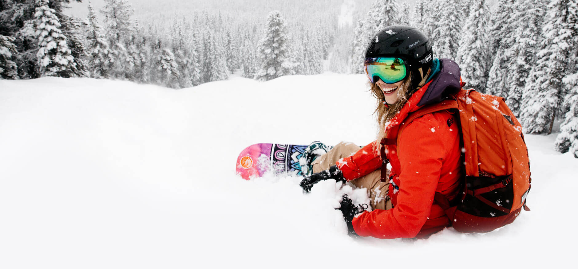 Imagery of a woman snowboarder on the Marmot Basin mountain, sitting in deep powder snow with a big smile on her face